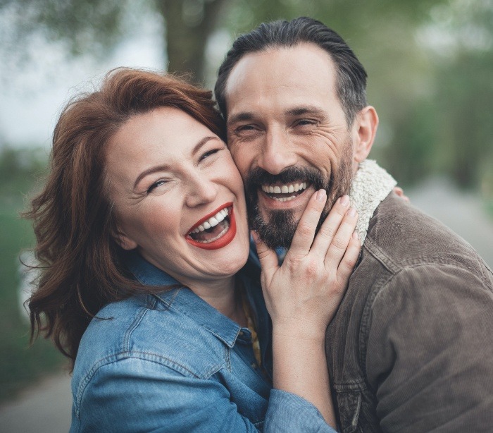 Man and woman sharing healthy smiles after dental implant tooth replacement
