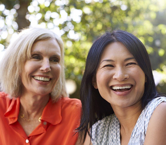 Two women with healthy smiles after bone grafts and dental implant tooth replacement