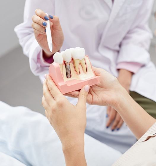 Dentist and patient looking at model dental implant tooth compared to natural tooth