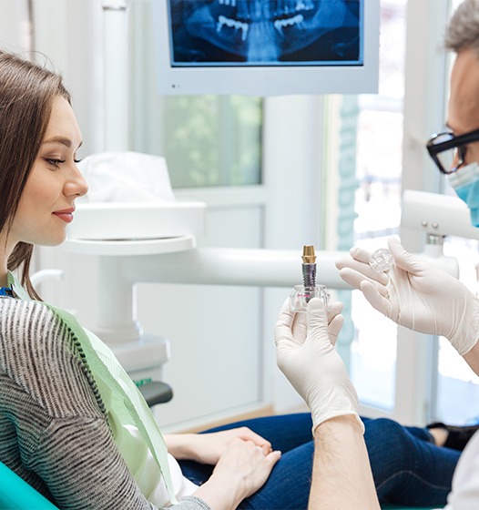 Dentist showing patient a model dental implant supported dental crown
