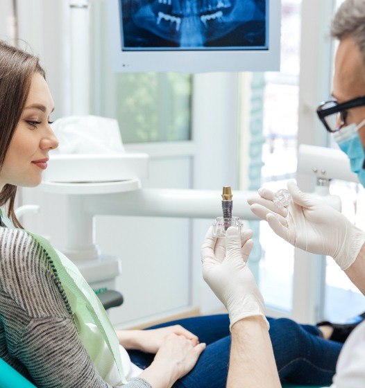 Dentist showing patient a model dental implant supported replacement tooth